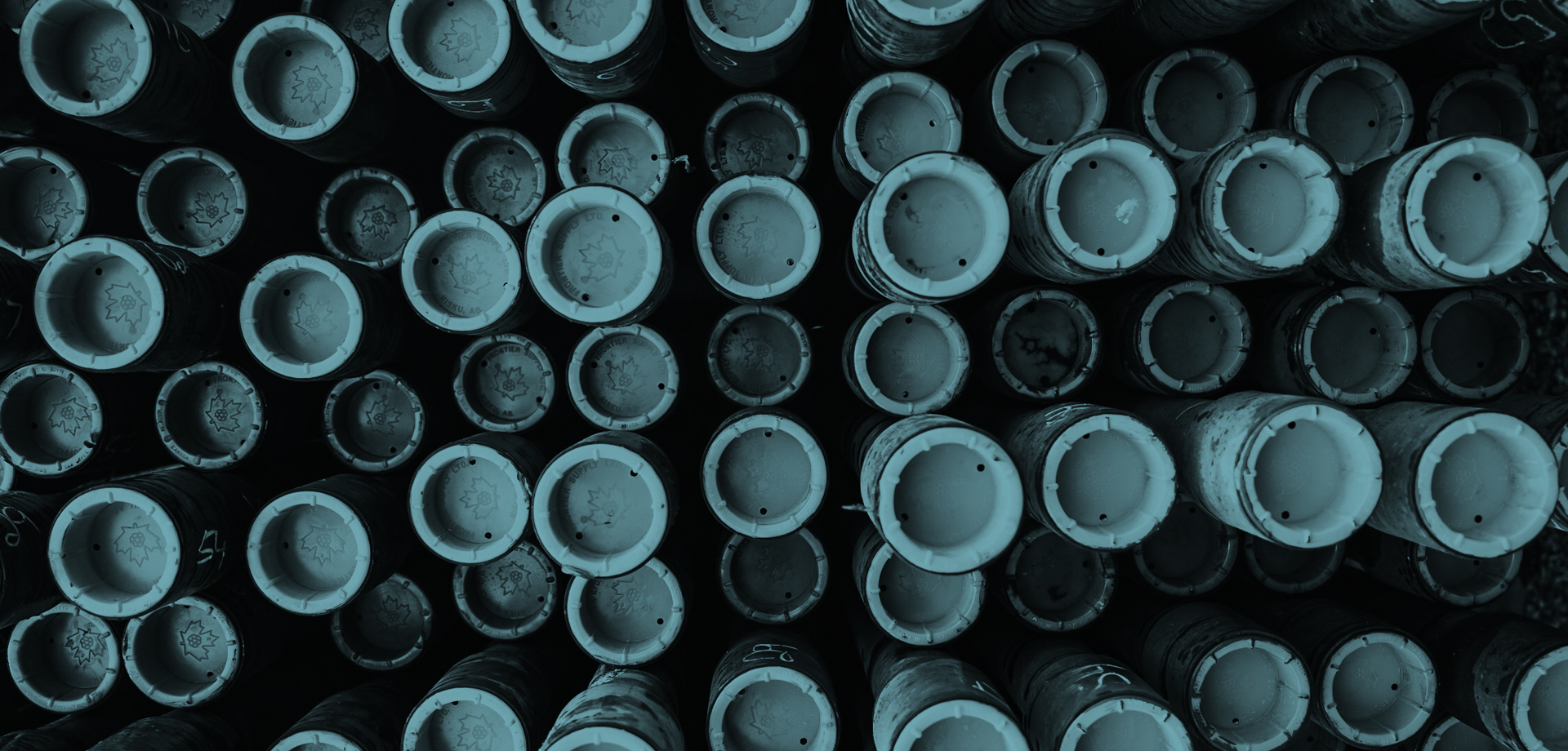 A close-up of the ends of approximately 60 heavy-duty oilfield pipes, each one plugged up with a cap marked with the Canadian maple leaf.