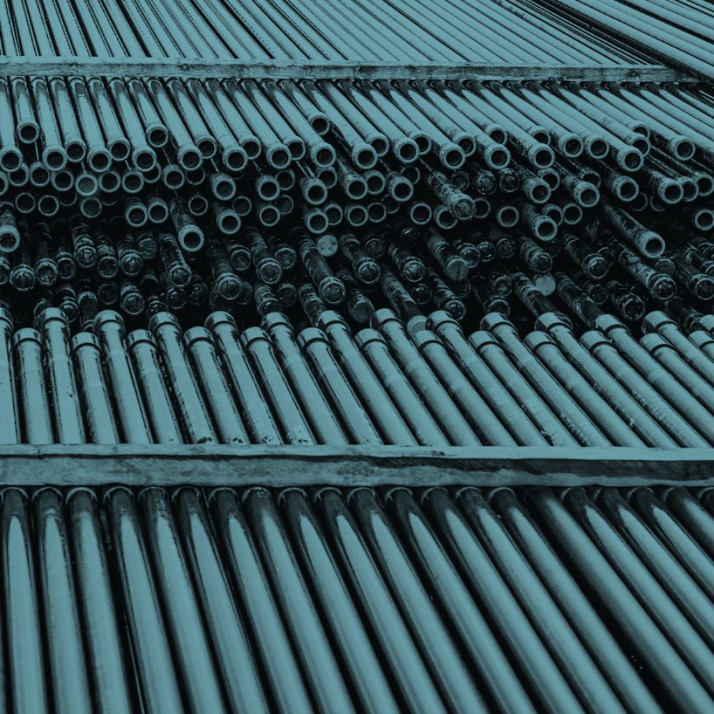 Dozens of long and slender heavy-duty oilfield pipes sit arranged in stands in an industrial yard.